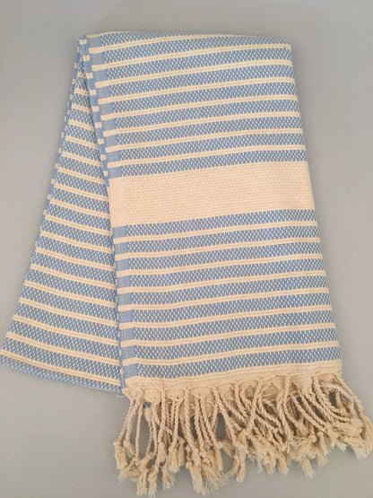 Light blue and cream striped Turkish towel with fringed edges, folded on a neutral background.