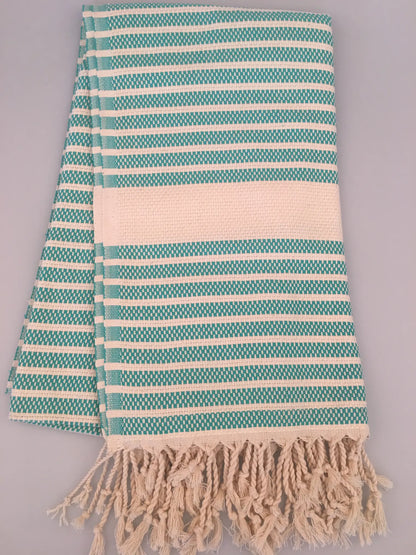 Turquoise and white striped Turkish towel with fringe edges, laid flat on a light background.