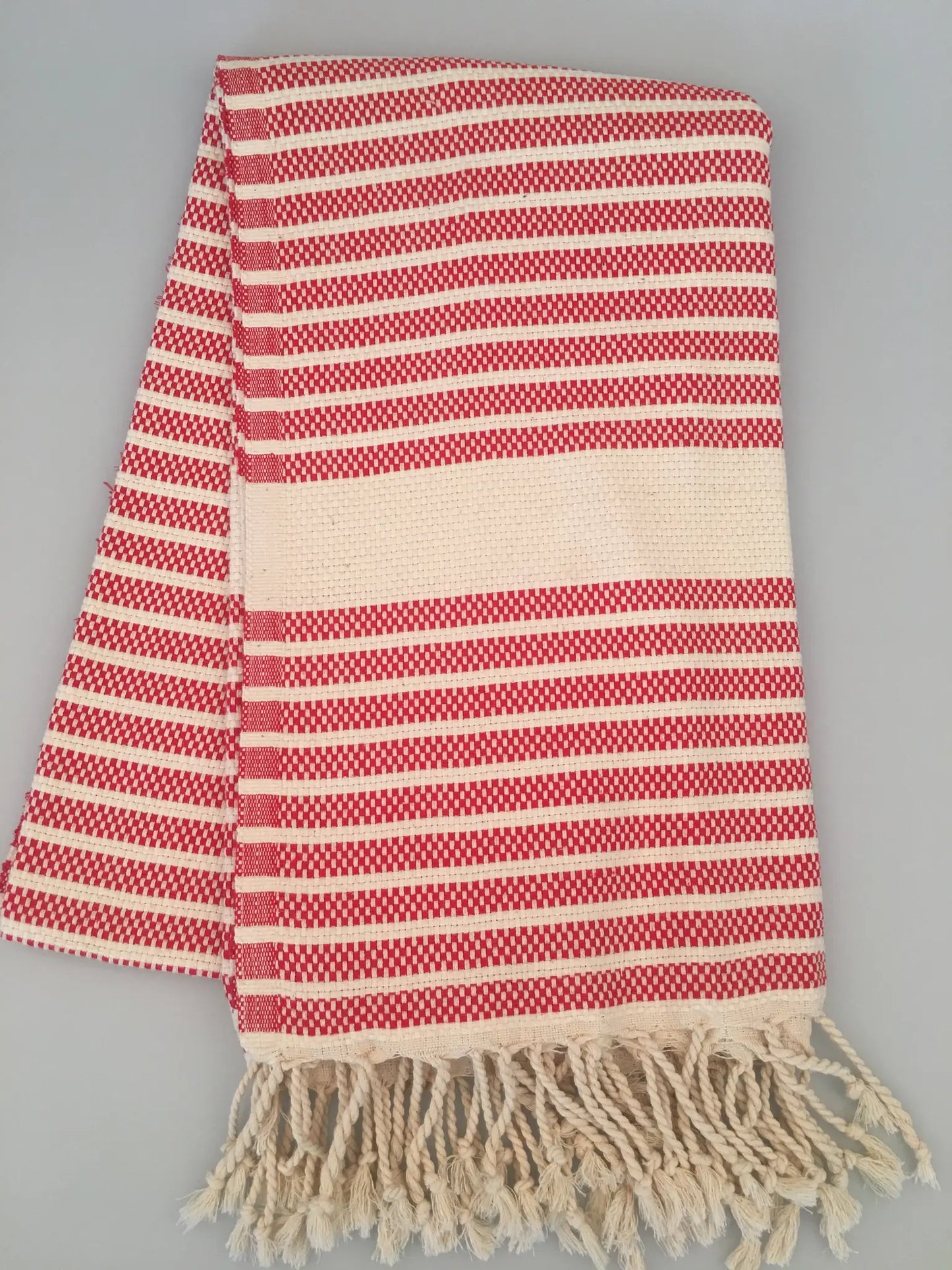 Red and white striped Hittite Turkish towel with fringed edges, laid flat on a gray background.