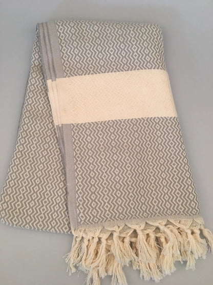 "Gray and white Turkish towel with geometric pattern, featuring fringed edges and a solid band at the center."