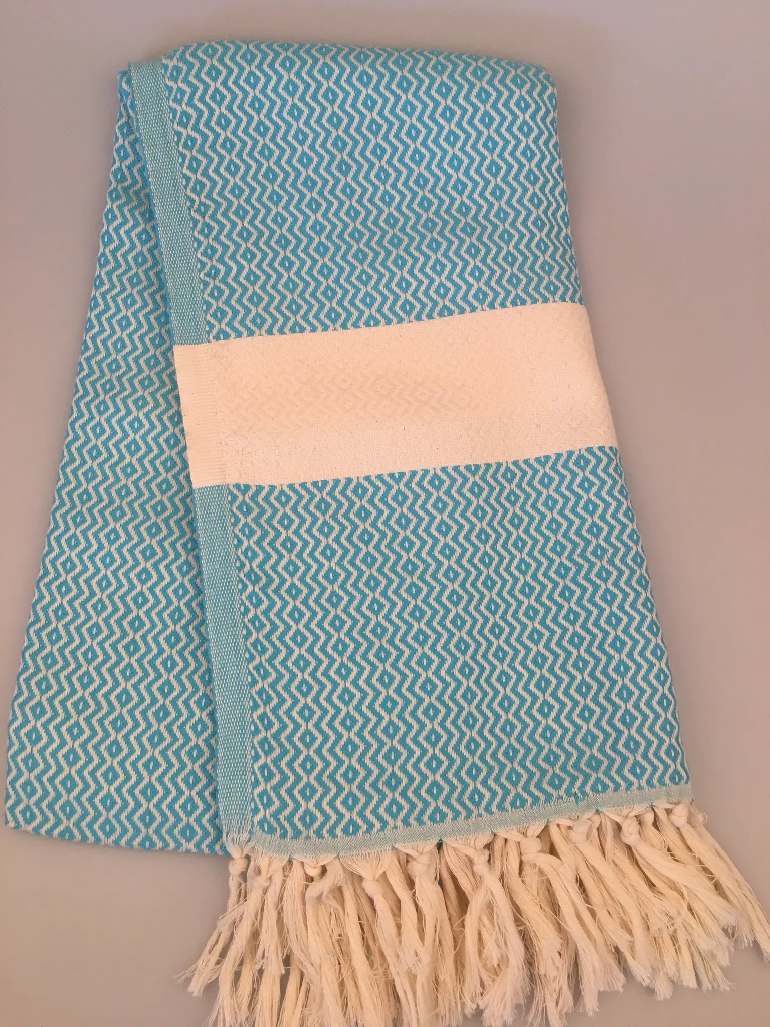 Turquoise Turkish towel with a white band, featuring a textured pattern and fringed edges, folded neatly.