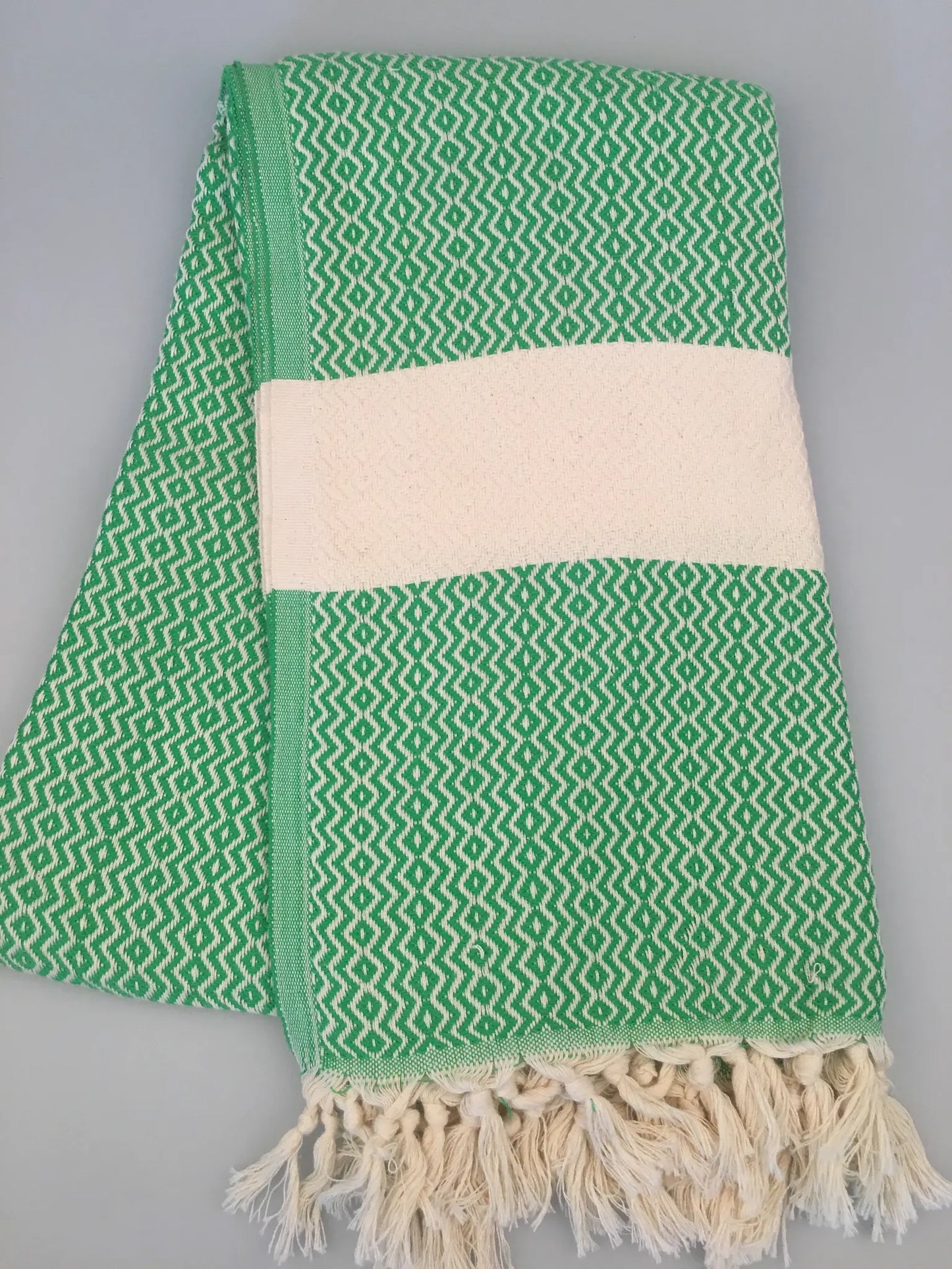 Green Turkish towel with a geometric pattern, featuring a cream-colored band and fringed edges, laid flat.