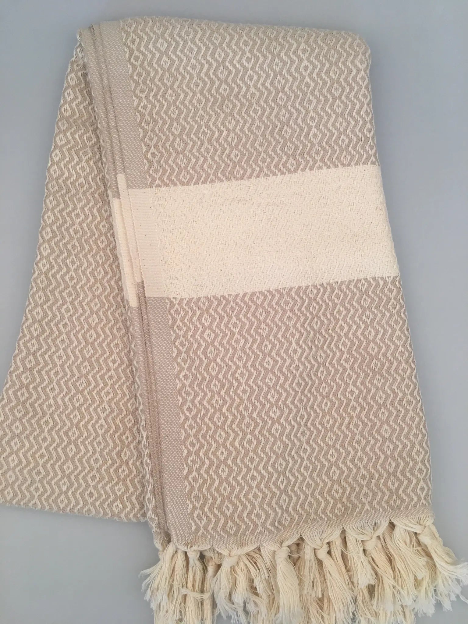 "Beige Turkish towel with a geometric pattern, cream stripes, and fringe edges, folded on a light background."