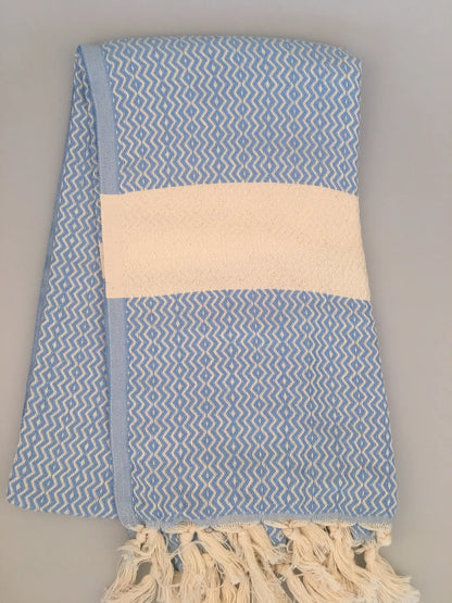 Light blue Turkish towel with a white striped band, featuring a textured weave and fringed edges.