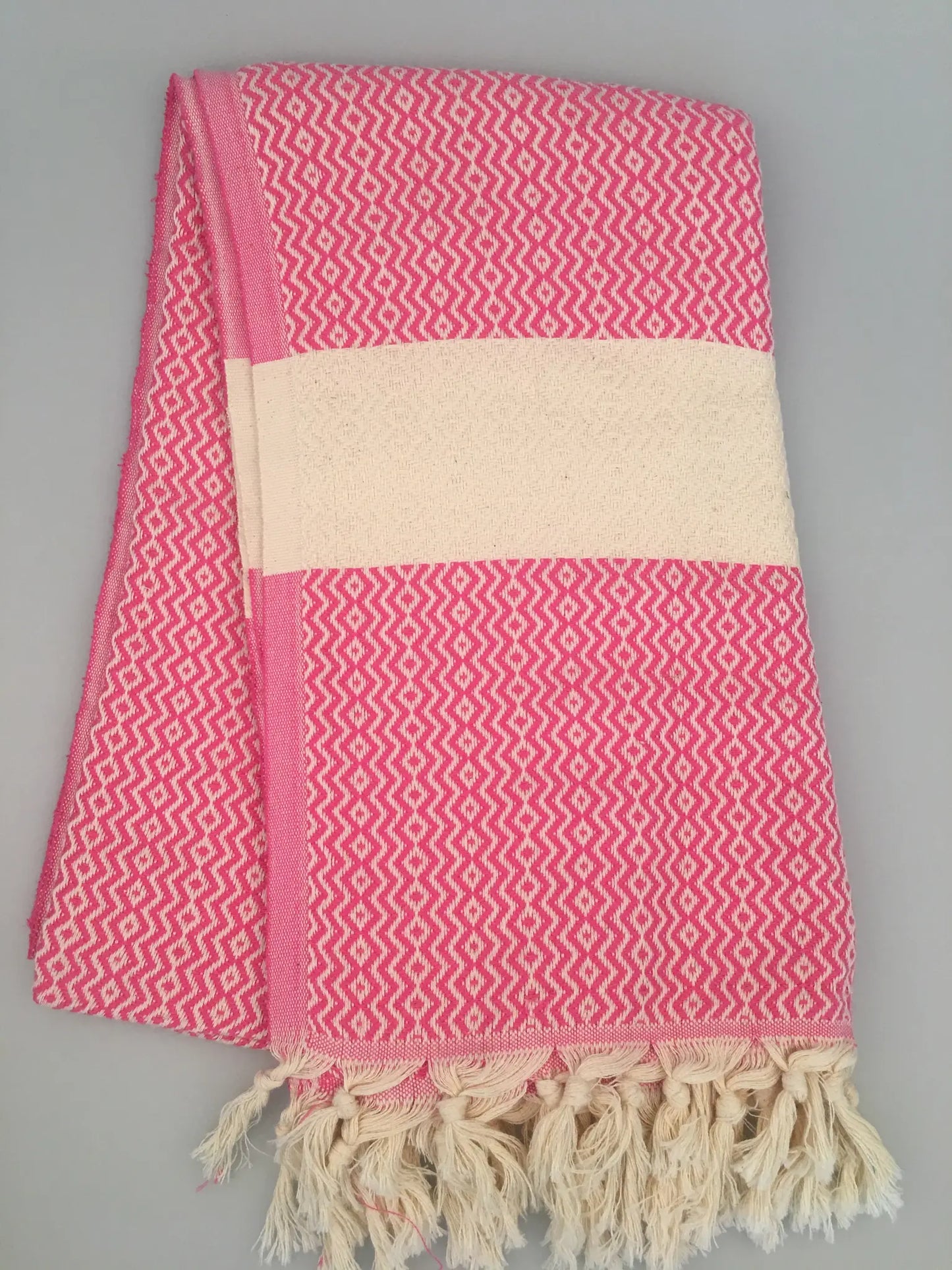 "Pink and white Turkish towel with zigzag pattern and fringed edges, folded view on light background."