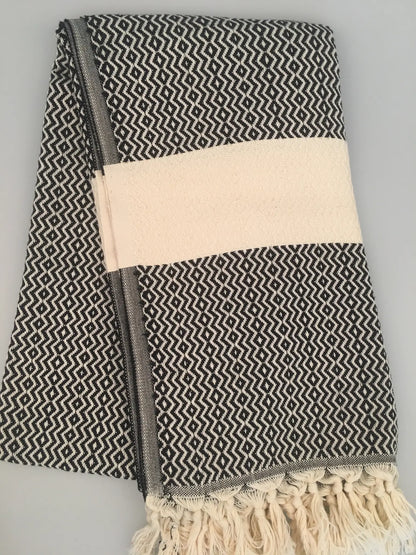 "Black and white patterned Turkish towel with cream stripe and fringed edges, folded neatly."