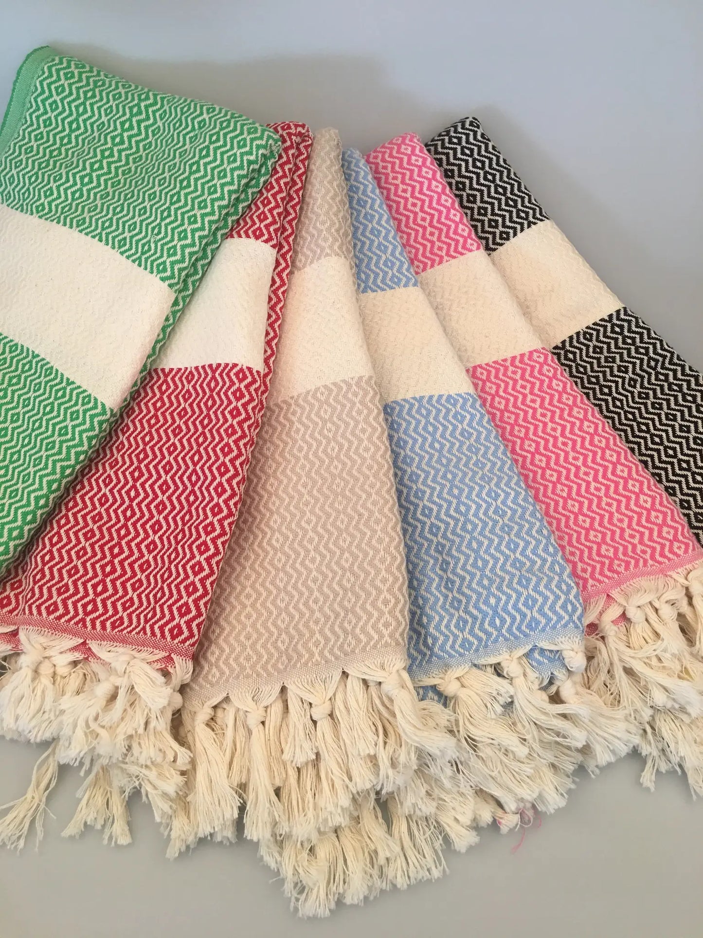 "Lycia Letoon Turkish towel in green, red, pink, blue, and black patterns, with fringed edges, laid flat on a light backgroun