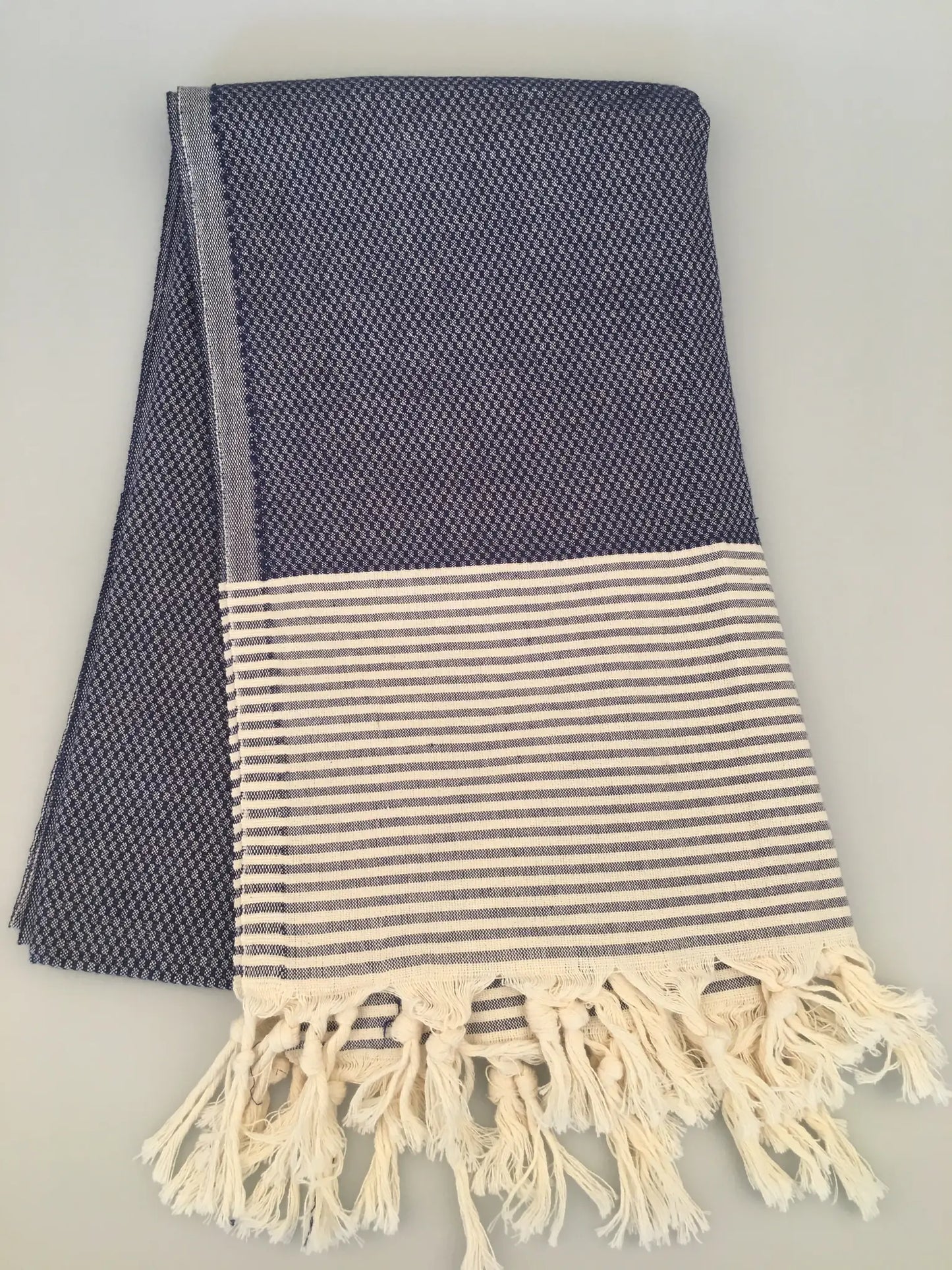 "Navy blue peshtemal towel with textured pattern and white striped border, fringed edges, folded view."
