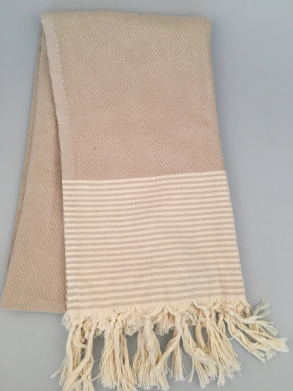 "Beige Miletus Turkish towel with textured weave and striped hem, featuring fringed edges, laid flat."