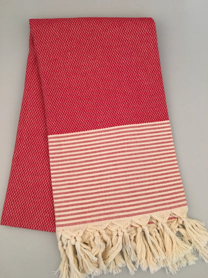 Red Turkish towel with textured pattern, featuring a striped white and red border and fringed edges, laid flat.