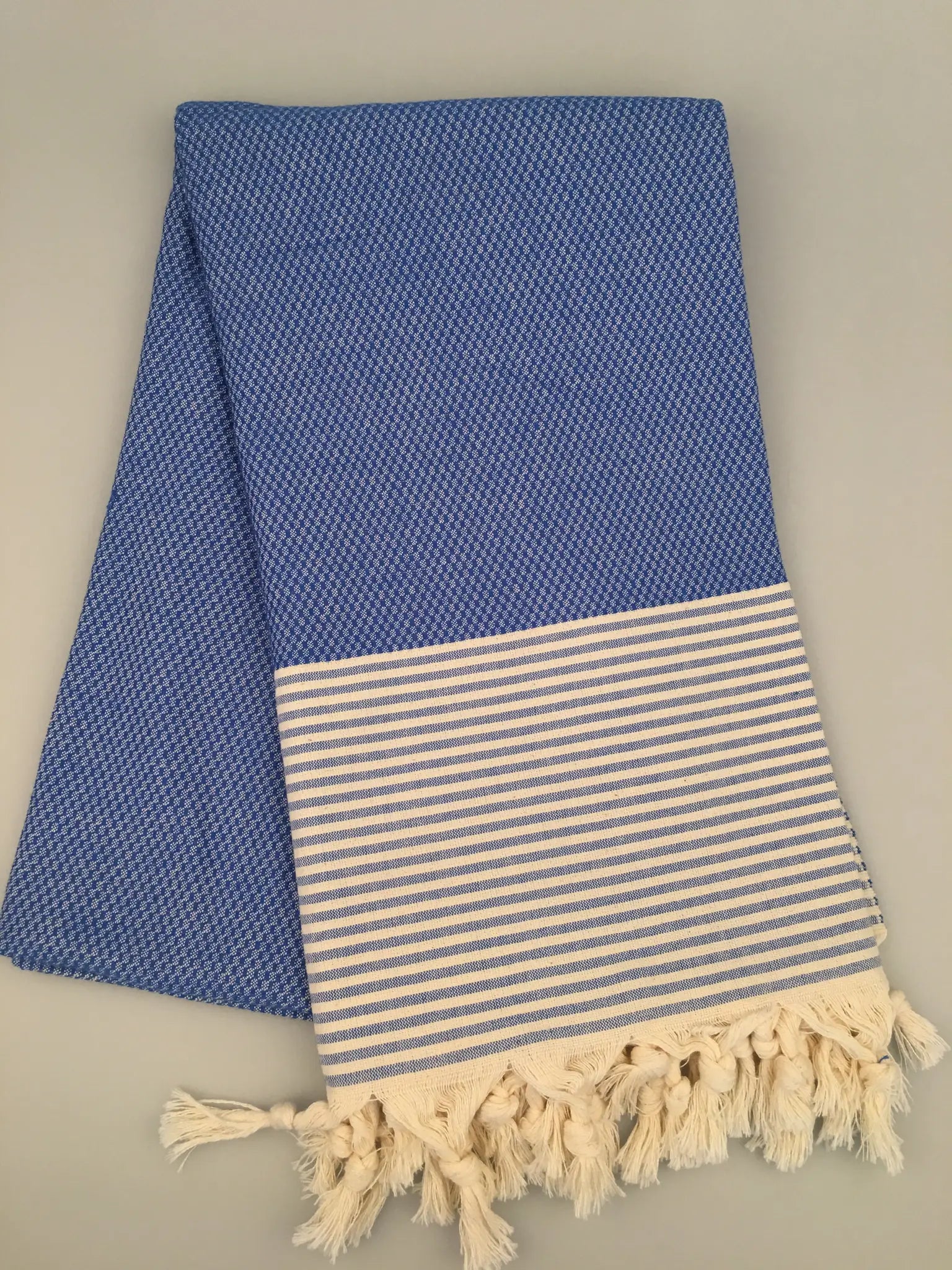 "Blue Miletus Turkish towel with textured weave and striped white hem, featuring cream fringes at the bottom."