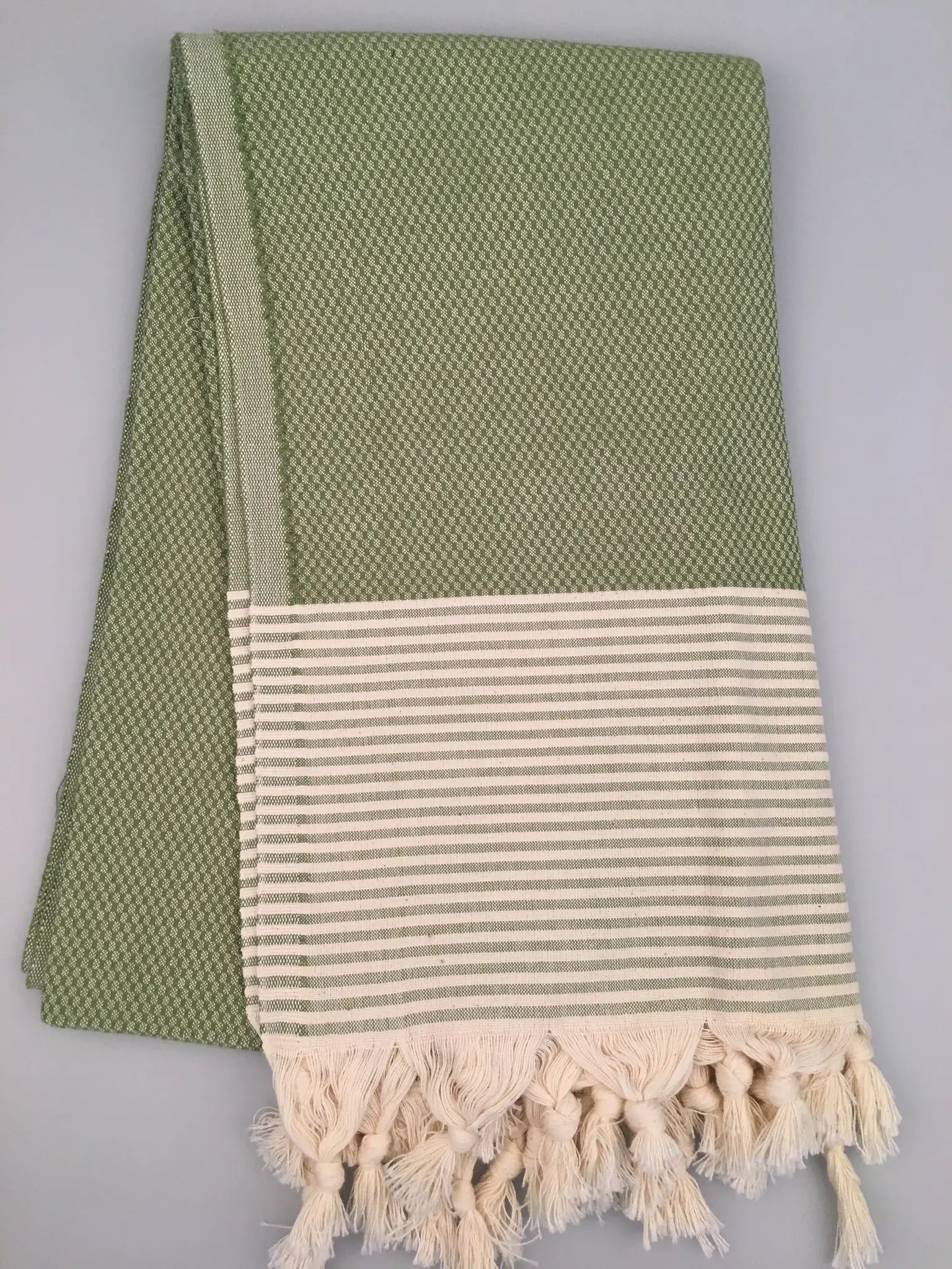 "Light green Turkish towel with textured weave and white striped border, finished with cream fringes."