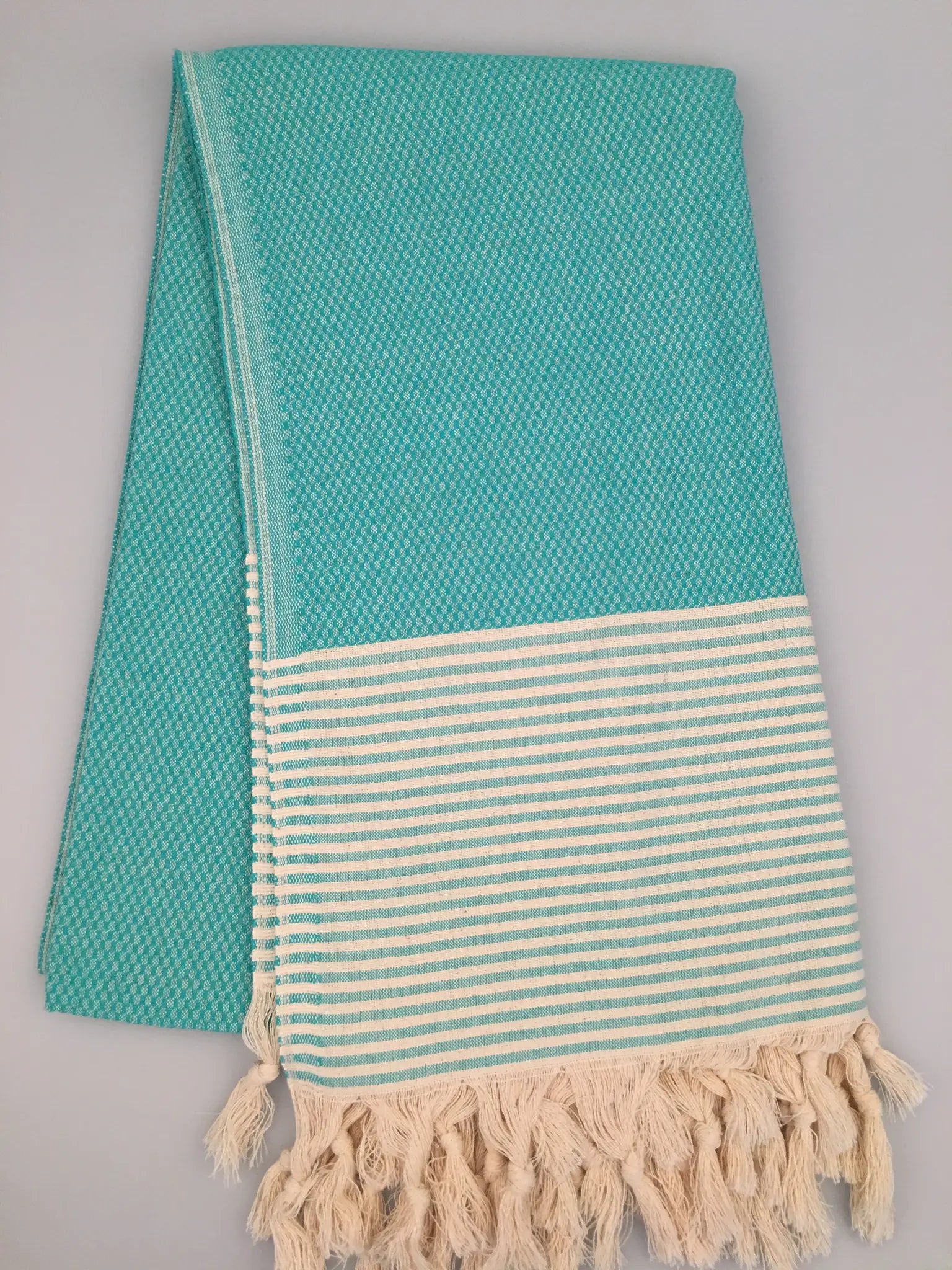 Turquoise Turkish towel with a textured weave, featuring a striped cream and turquoise border and fringed ends.
