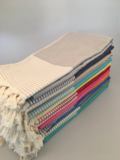 "Stack of Miletus Turkish towels in various colors, featuring striped patterns and fringed edges, side view."