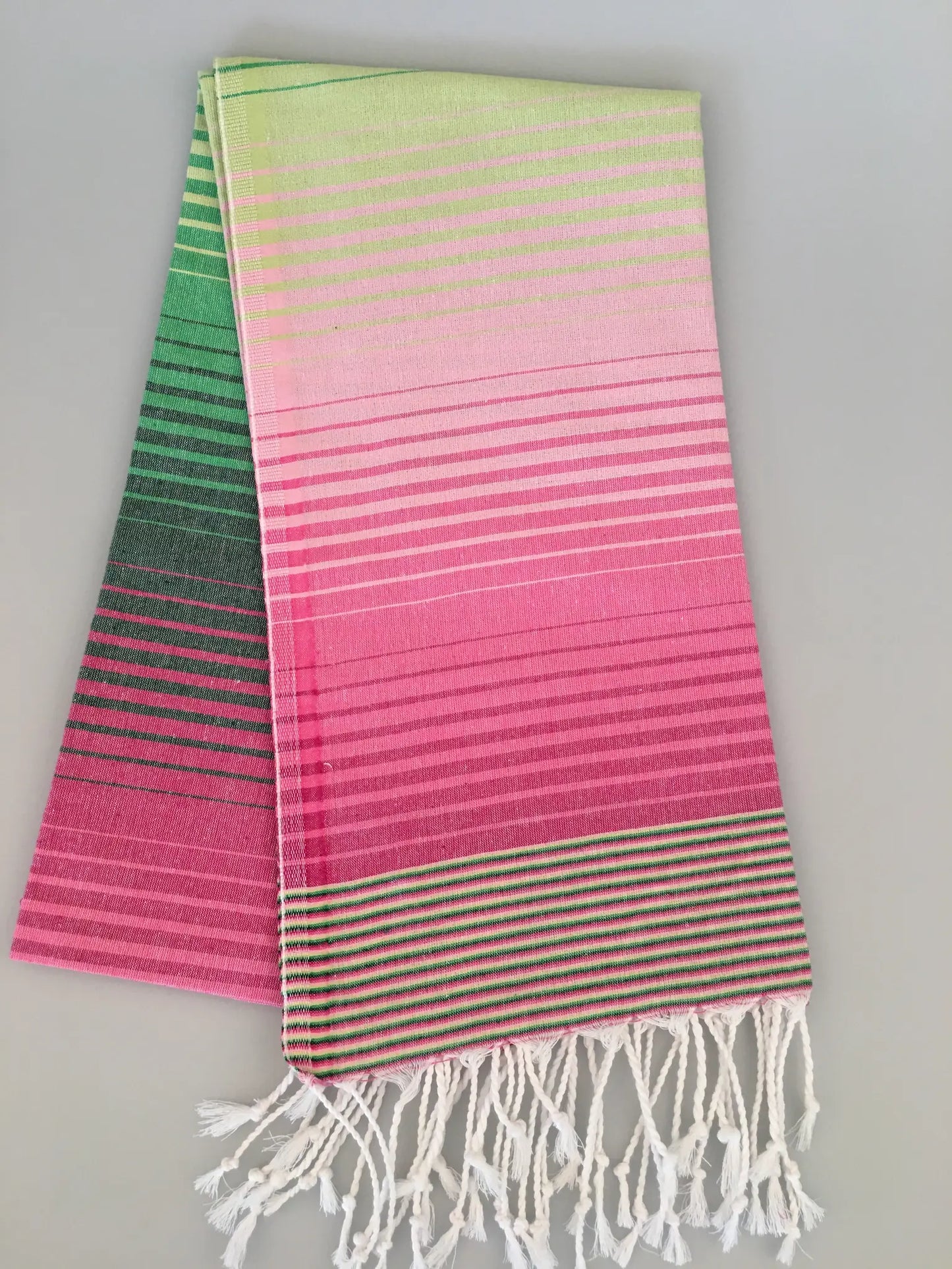 "Striped pink and green Turkish towel with fringed edges, displaying a gradient pattern from dark green to light pink."