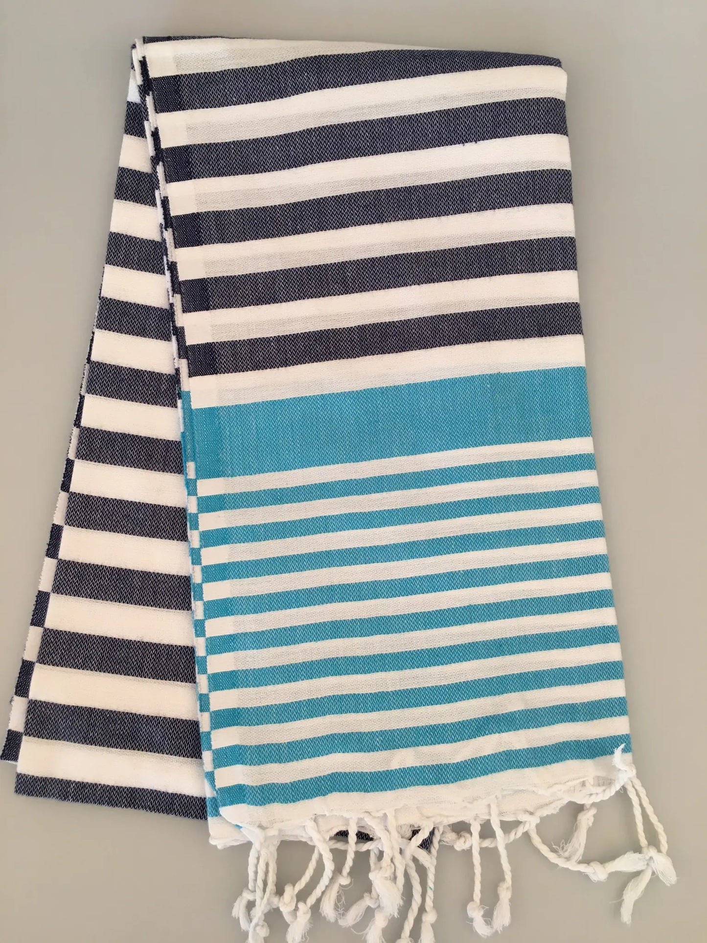 "Striped Tlos Turkish towel peshtemal in navy and white with a turquoise section, fringed edges."