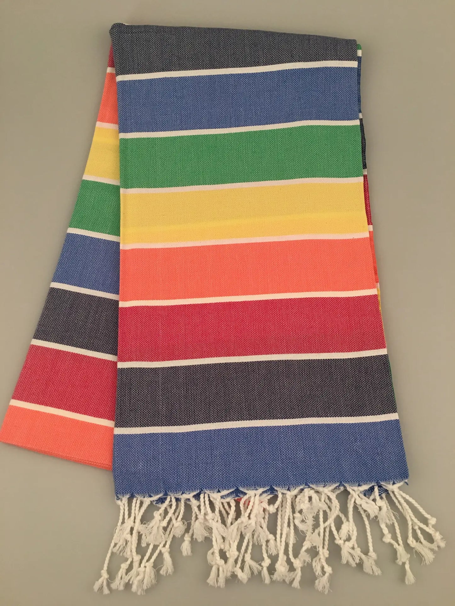 Colorful Iasos Turkish towel with horizontal stripes in blue, green, yellow, red, and orange, featuring white fringes at the 