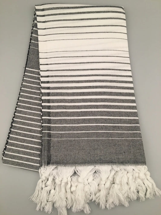 "Telmessos Turkish towel peshtemal in gray and white stripes, featuring fringed edges, laid flat on a gray background."