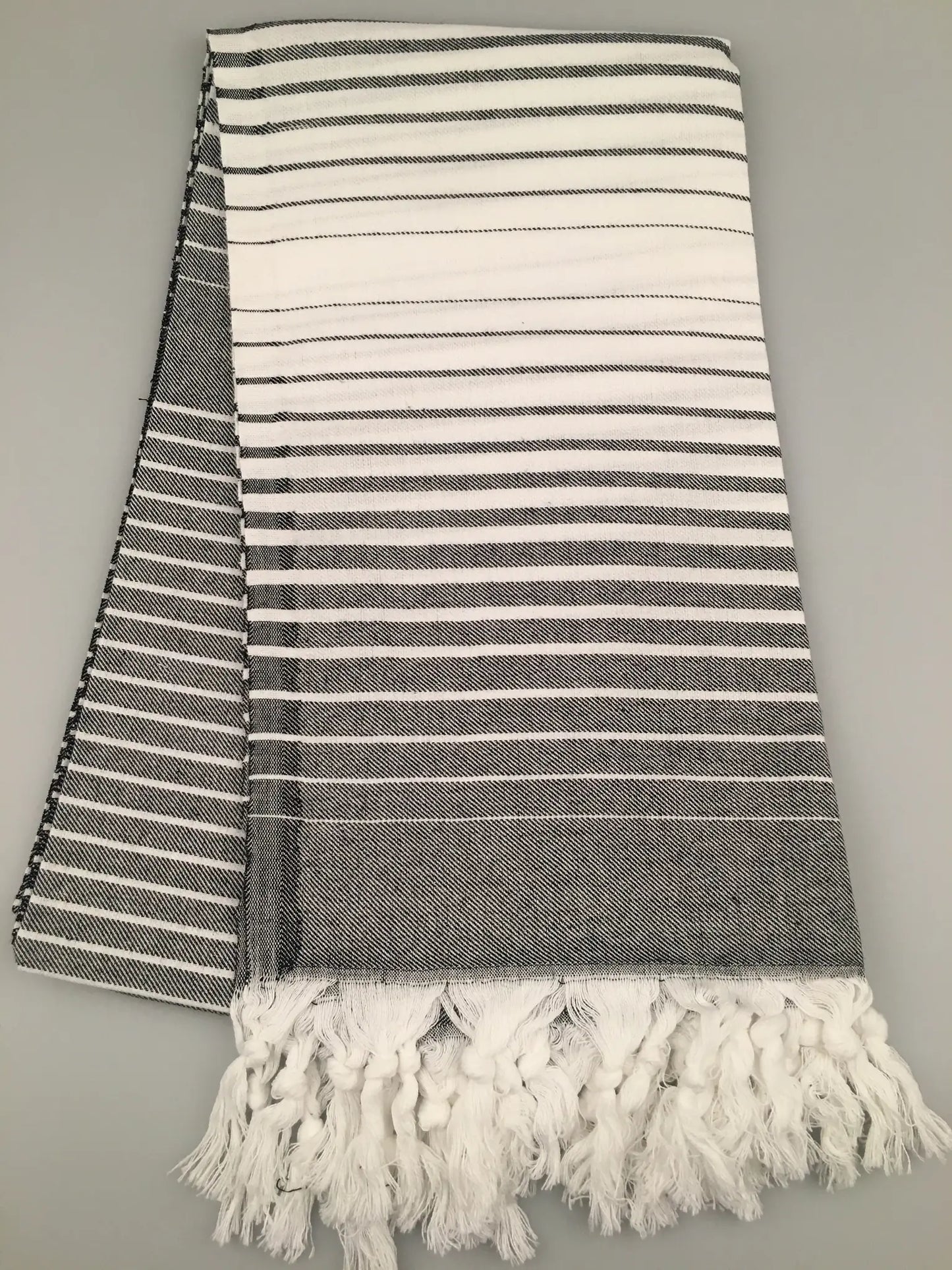 "Telmessos Turkish towel peshtemal in gray and white stripes, featuring fringed edges, laid flat on a light background."
