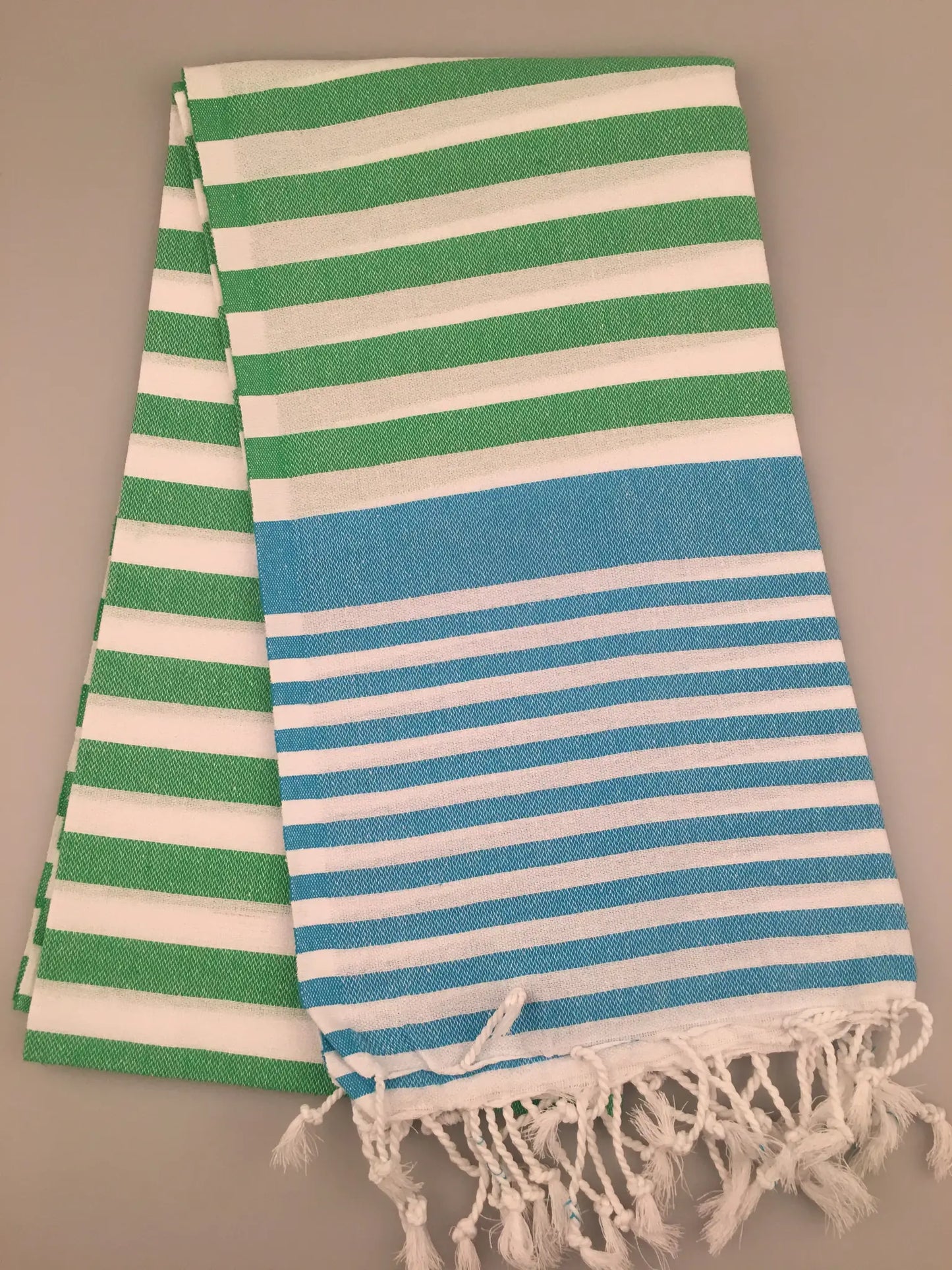 "Striped Turkish towel in green and blue with white stripes, featuring fringed edges, flat lay view"