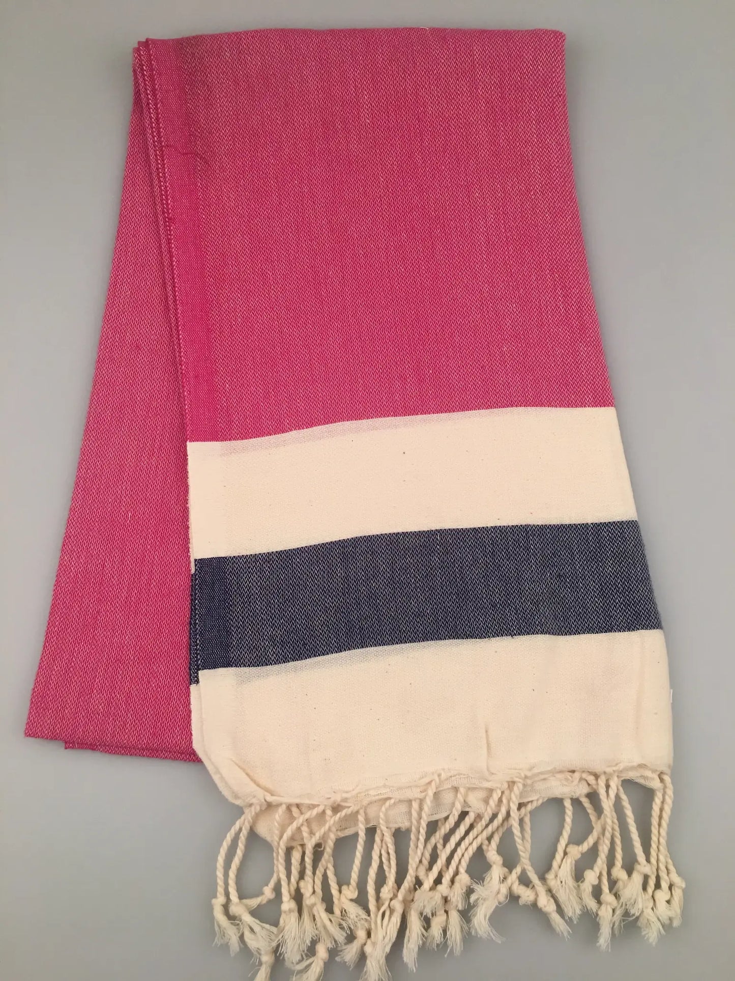 "Blaundus Turkish towel peshtemal in pink with a cream and navy striped border, featuring fringed edges."