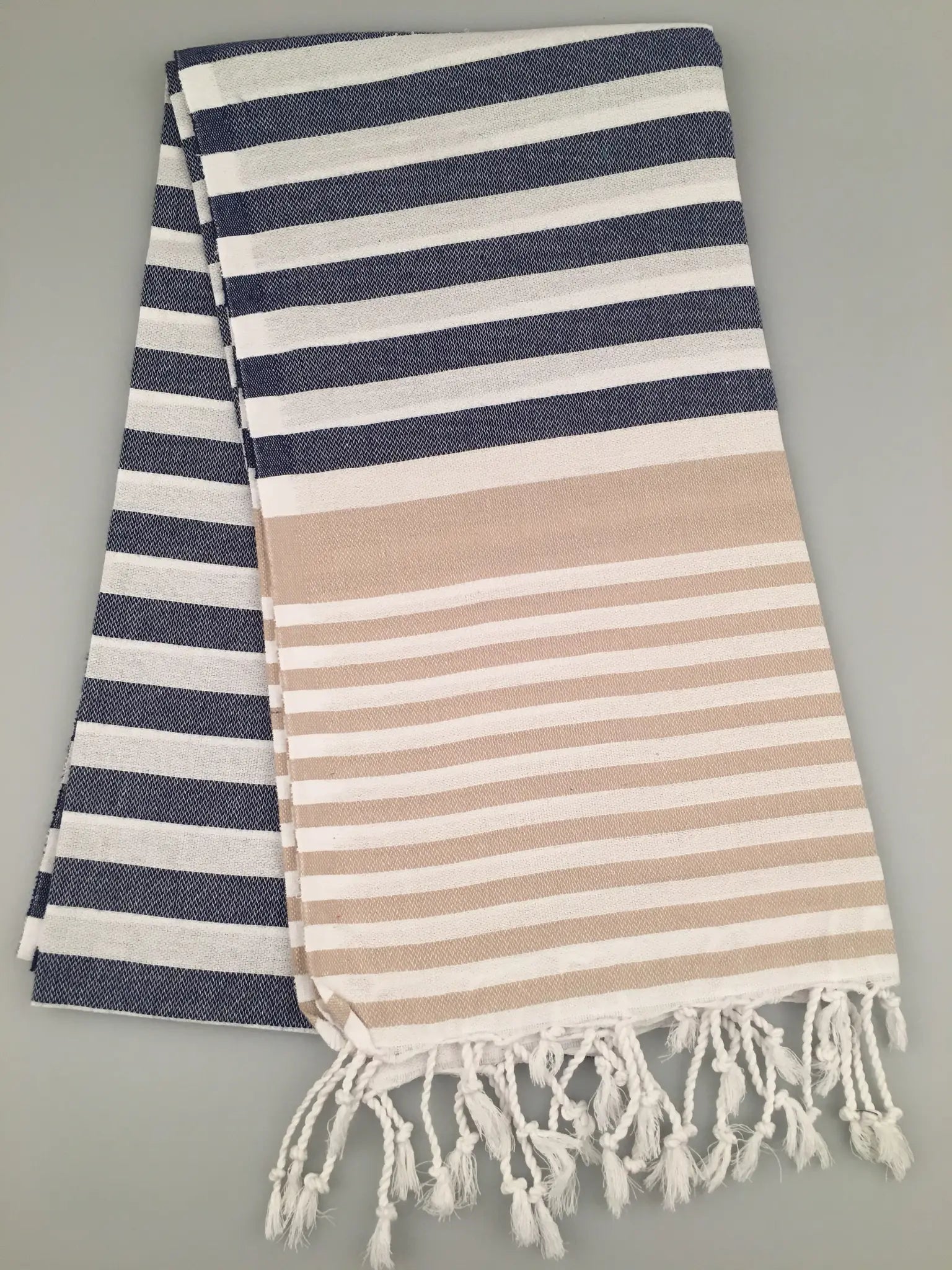 "Blue and white striped Turkish towel with beige horizontal band and fringed edges, folded flat"