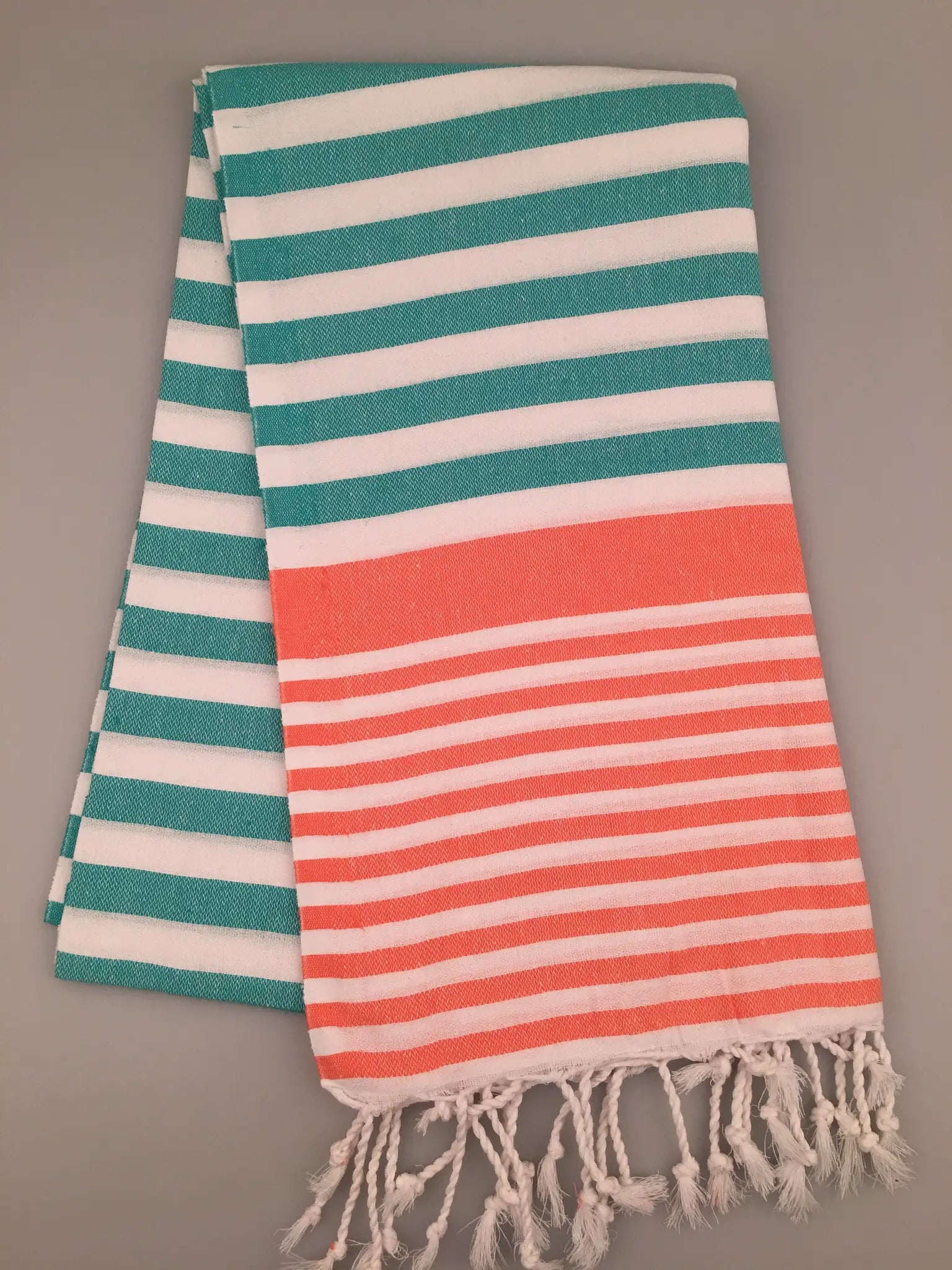 "Striped Turkish towel in turquoise and white with an orange band, featuring fringed ends, folded view."