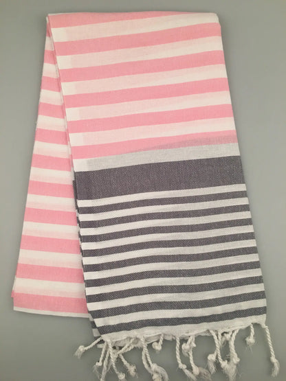 Pink and white striped Tlos Turkish Towel peshtemal with gray and white stripes at the bottom, fringed edges, laid flat.