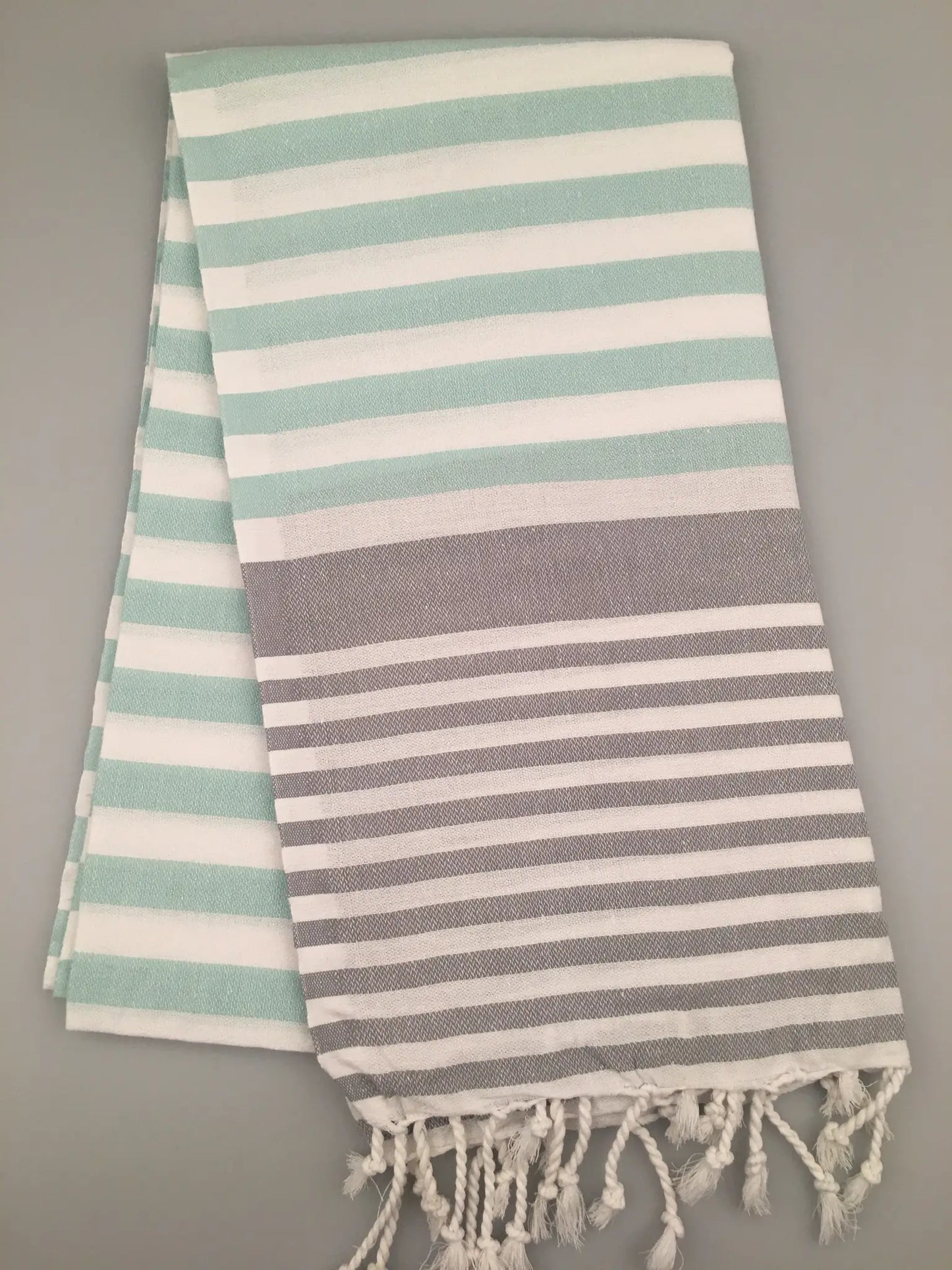 "Striped Tlos Turkish towel peshtemal in mint green and gray, featuring fringed edges, flat on a light background."