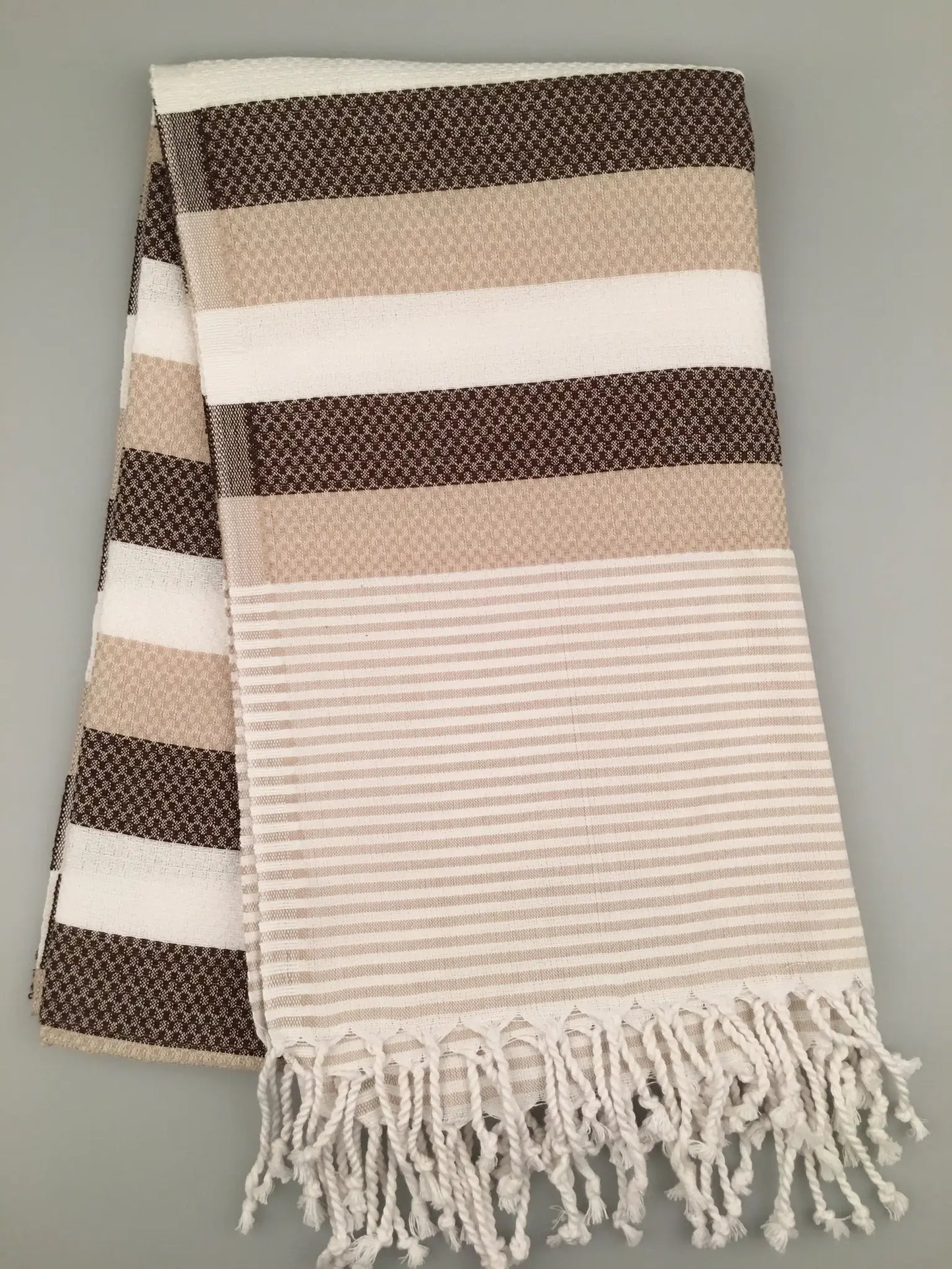 "Brown and beige striped Turkish towel with textured patterns and fringed edges, laid flat on a light background."