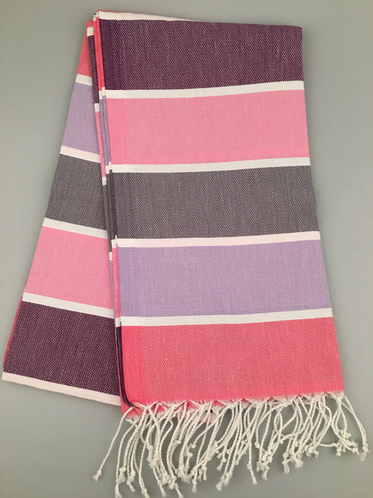 "Tripolis Turkish Towel Peshtemal in pink, purple, and gray stripes, folded with white fringe at the ends."