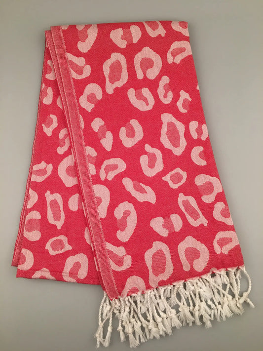 "Pink jacquard peshtemal with white leopard print and fringe edges, folded flat on a gray background."