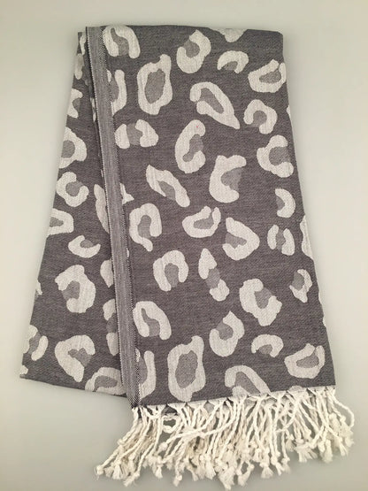 Gray Turkish towel with white leopard print pattern, fringed edges, folded flat on a light background.
