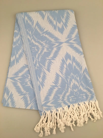 "Light blue Jacquard Turkish towel with white geometric pattern and fringed edges, displayed on a neutral background."