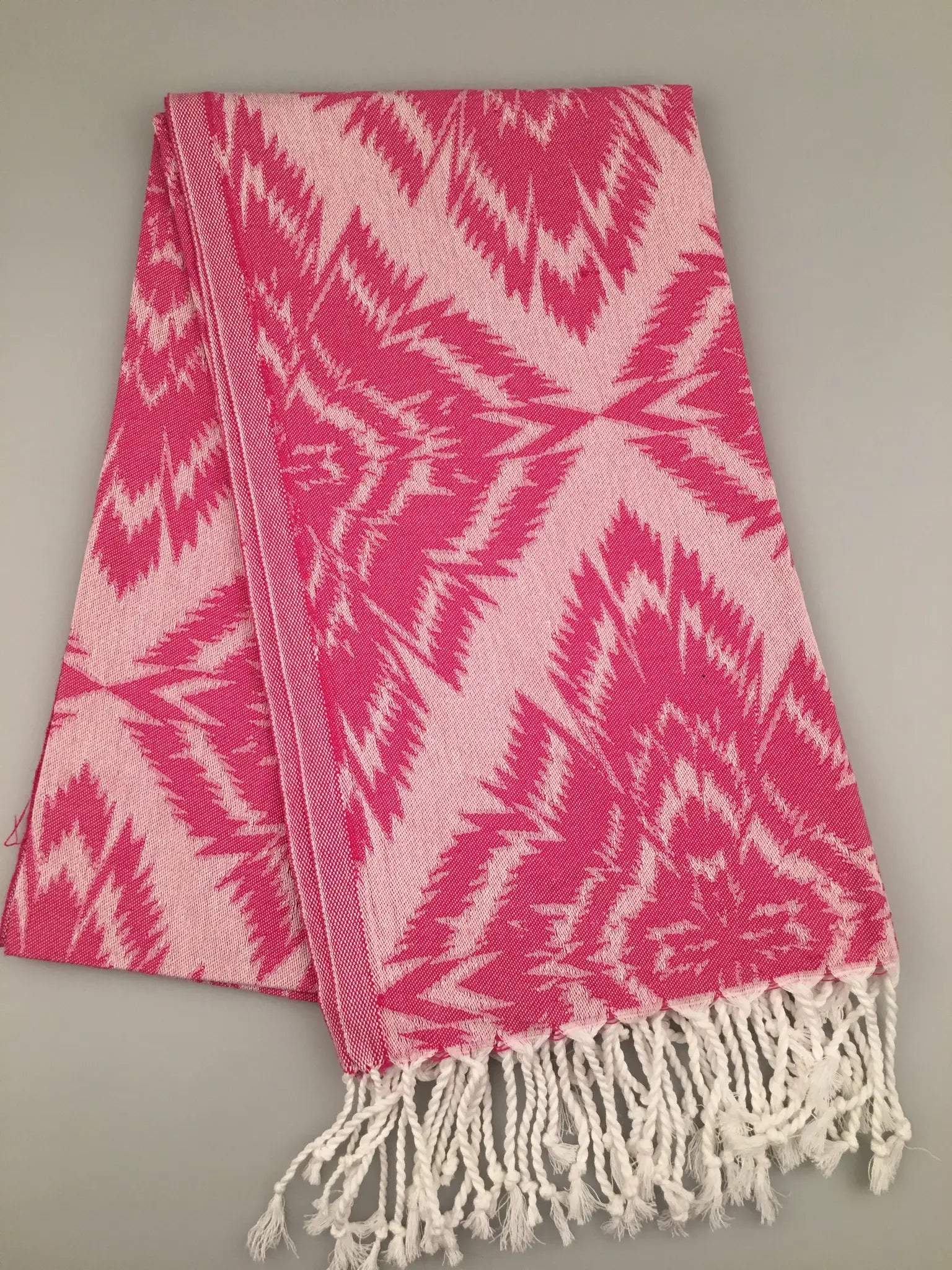 "Pink and white jacquard peshtemal with a geometric pattern and fringed edges, laid flat on a neutral background."