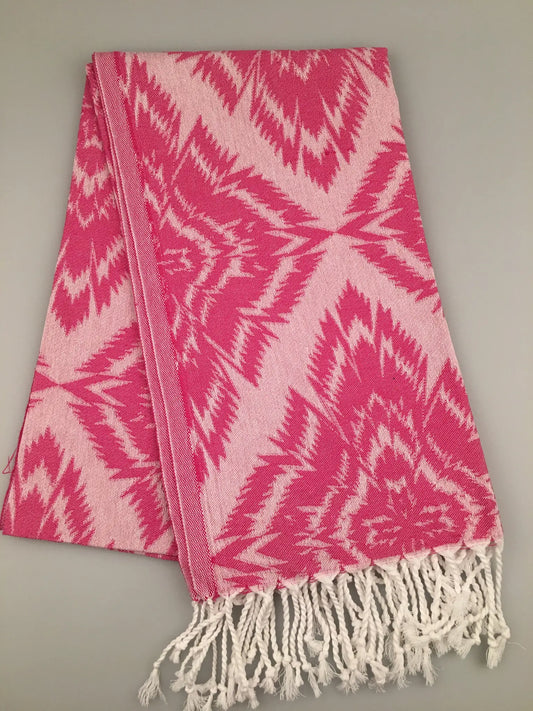 "Pink and white jacquard peshtemal with a geometric pattern and fringed edges, laid flat on a neutral background."