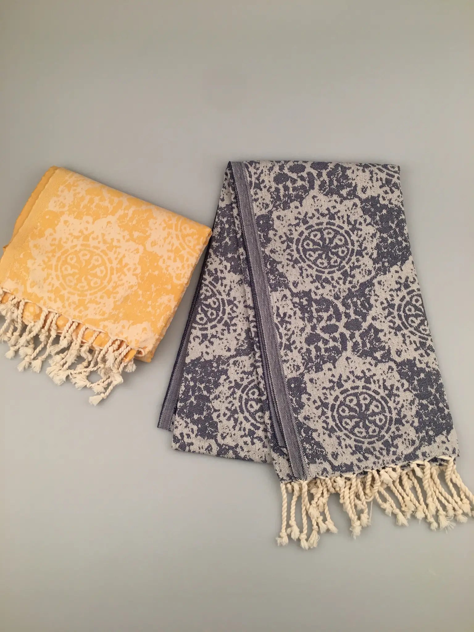 "Jacquard peshtemal towels in blue and gray with floral pattern, one folded in yellow, both with fringed edges."