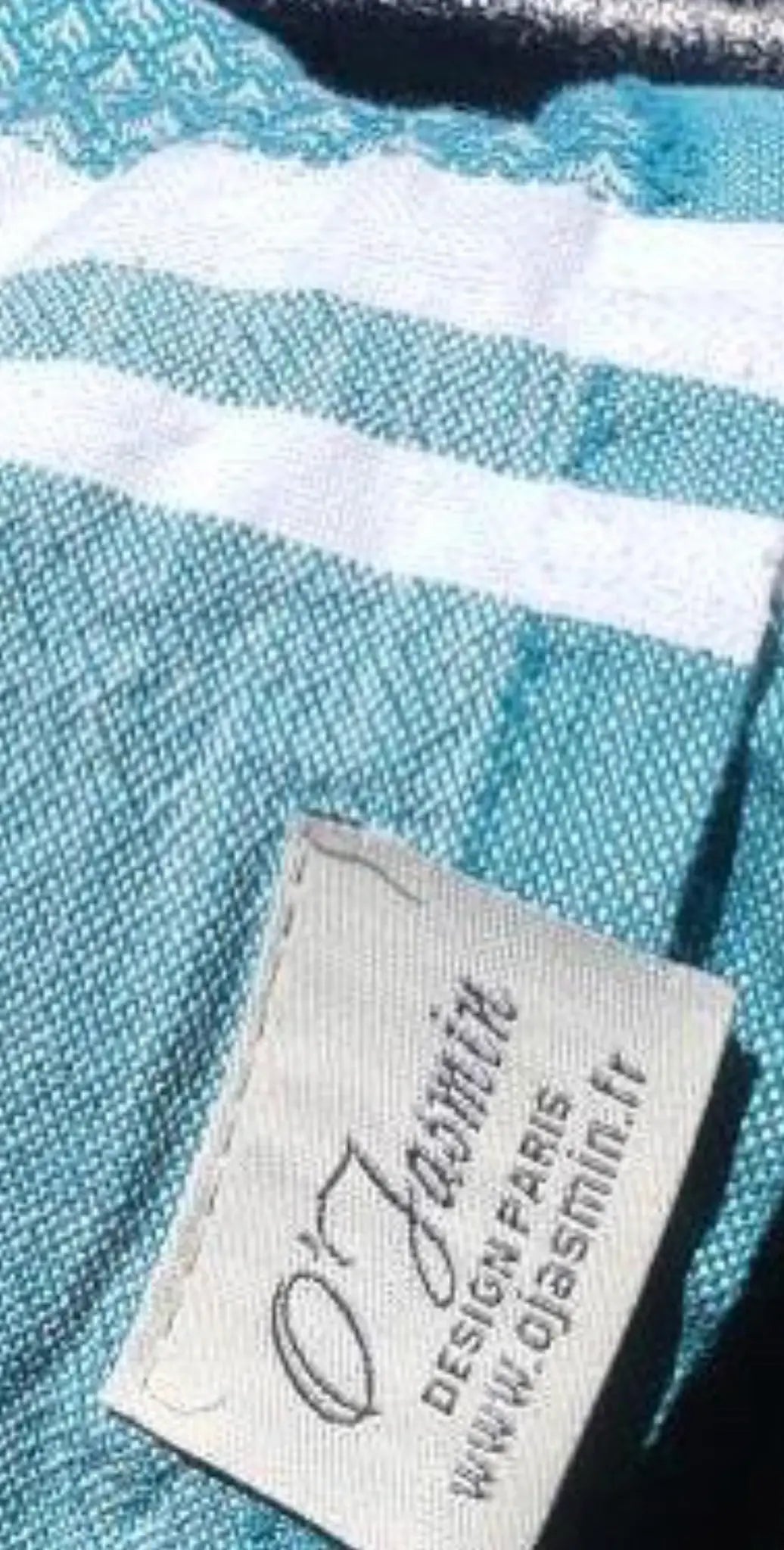 "White cotton label with blue text and woven texture, attached to a teal fabric with white stripes."