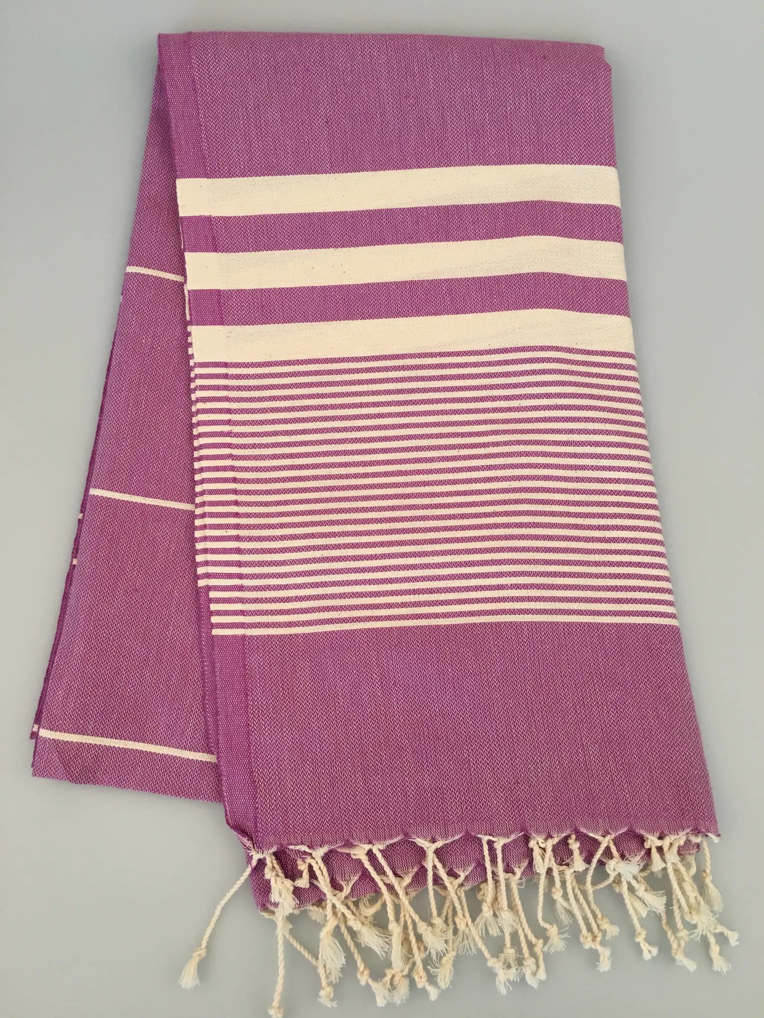 "Purple Turkish towel peshtemal with cream stripes and fringed edges, folded flat on a light background."
