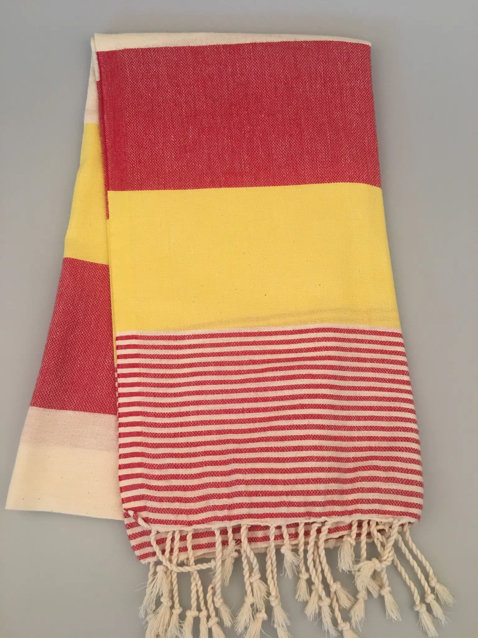 "Red and yellow striped Turkish towel with white fringes, folded and displayed on a light background."