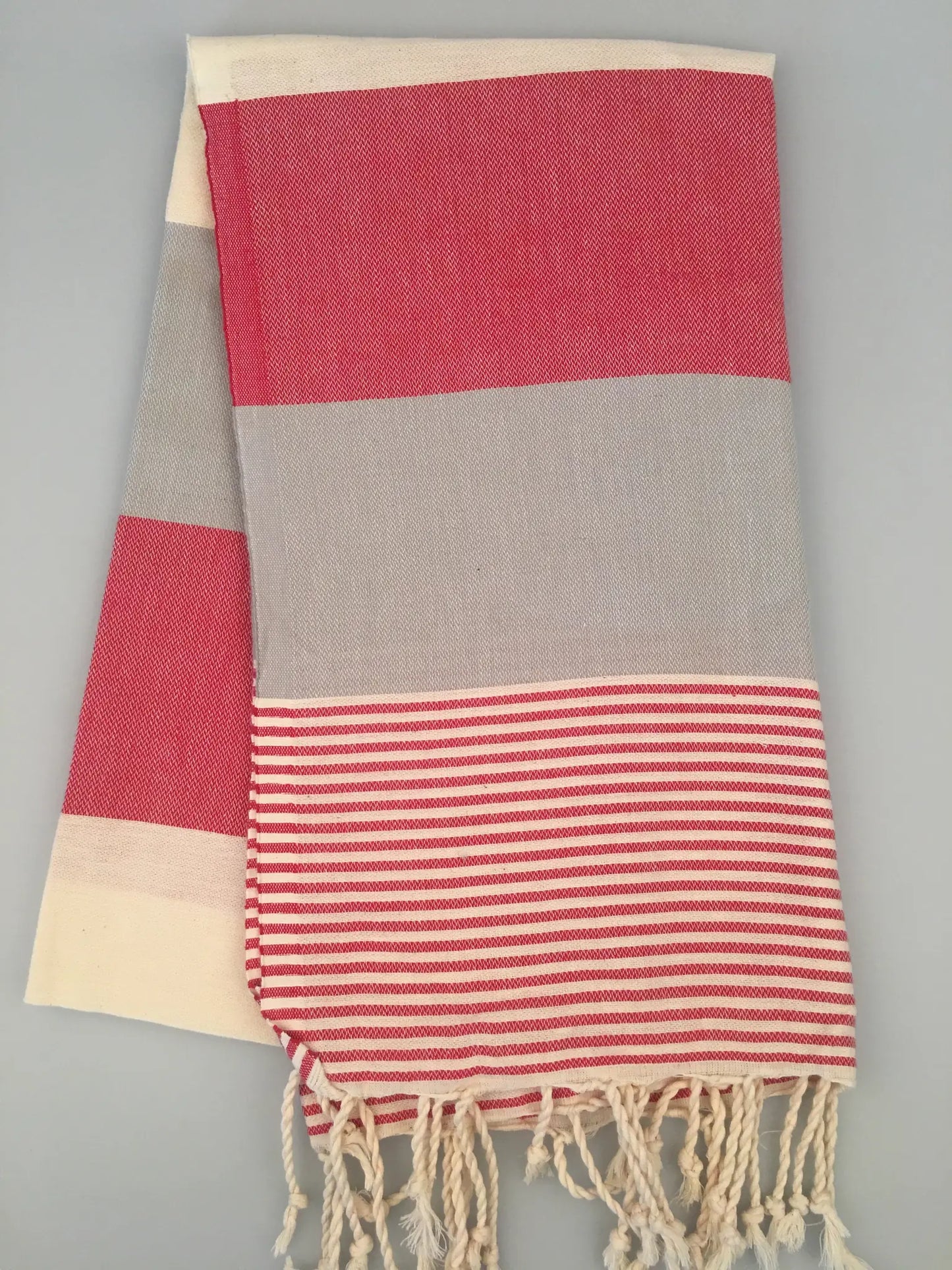 "Red and gray striped Lagina Turkish towel peshtemal with fringed edges, folded on a light background."