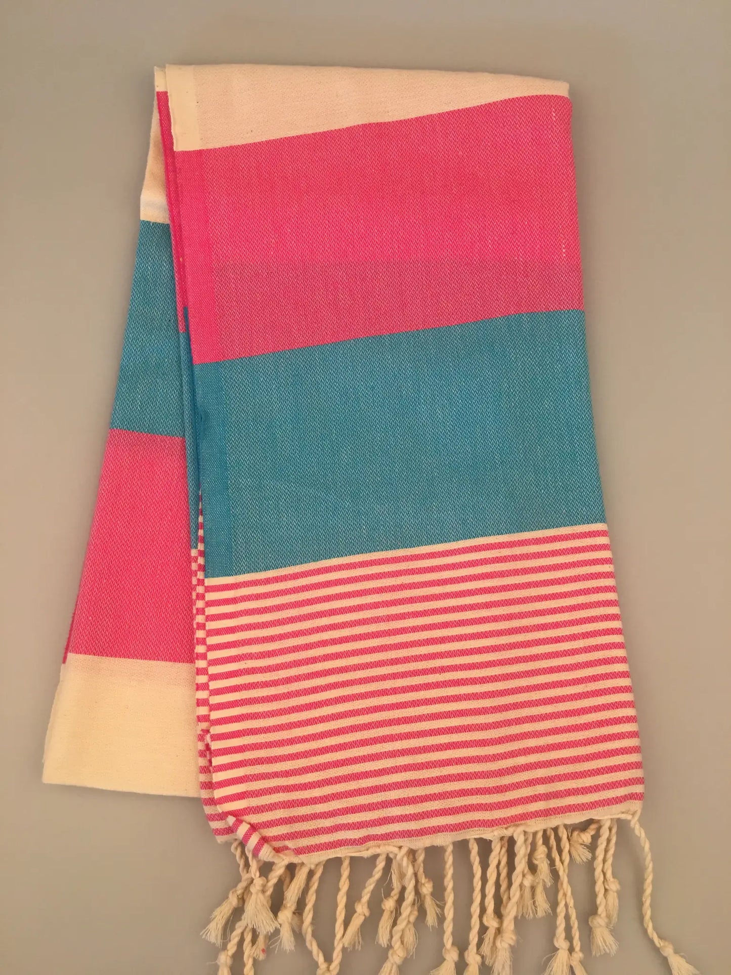 "Pink, teal, and cream striped Turkish towel with fringed edges, laid flat on a neutral background."