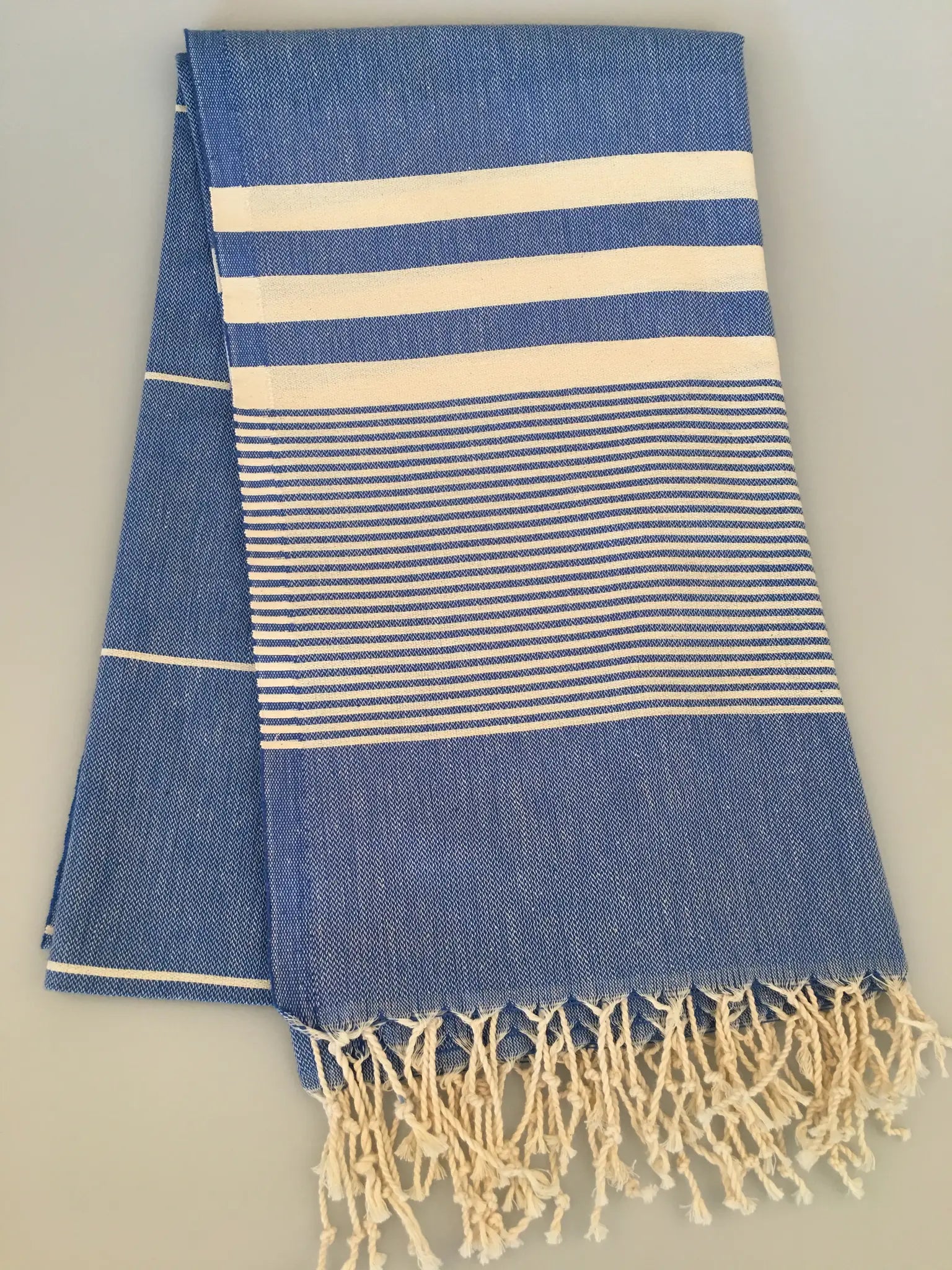 "Blue and white striped Turkish towel with fringed edges, folded neatly on a light background."