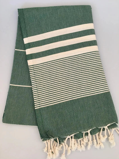 Green Turkish towel peshtemal with white stripes and fringed edges, folded neatly on a light background.