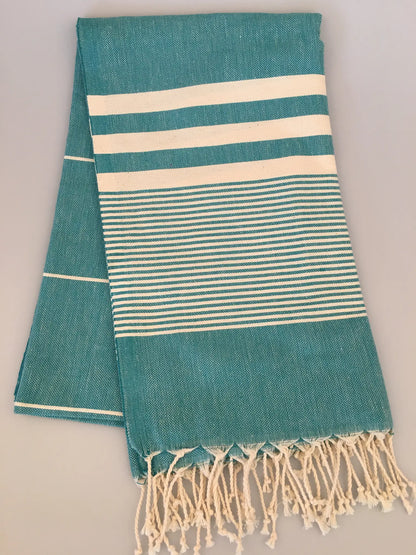 Teal Turkish towel with white stripes and fringed edges, folded neatly on a light background.