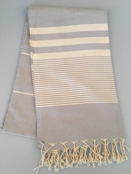 "Light gray Turkish towel with white stripes and fringed edges, folded view on a gray background."