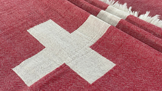Red fabric with a white cross pattern, textured weave, and fringed edges, close-up view.