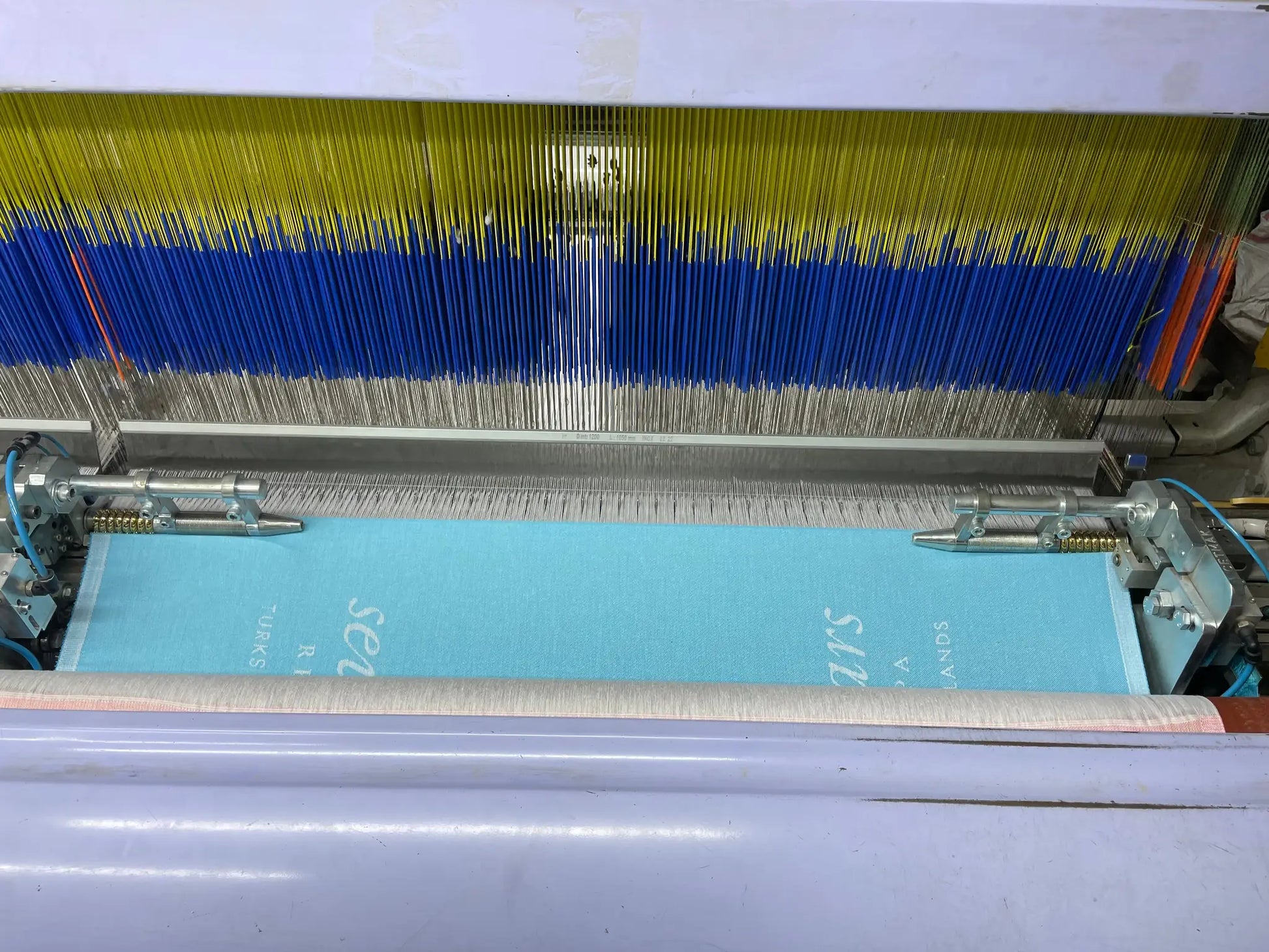 "Textile printing machine with blue and yellow threads, featuring a light blue fabric being processed."