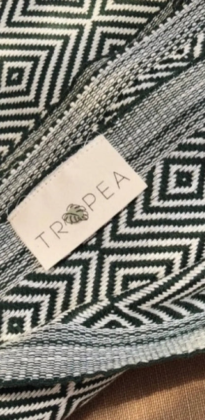"White fabric label with black geometric pattern and 'TROPEA' text, stitched onto a patterned green textile."
