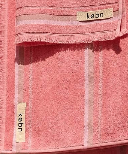 Two soft pink towels with striped design and fabric labels, one larger towel folded over a smaller one.